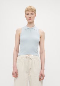 Top polo senza maniche di colore azzurro chiaro a coste con colletto e tre bottoni, abbinato a pantaloni larghi crema con vita elastica e cordino.
