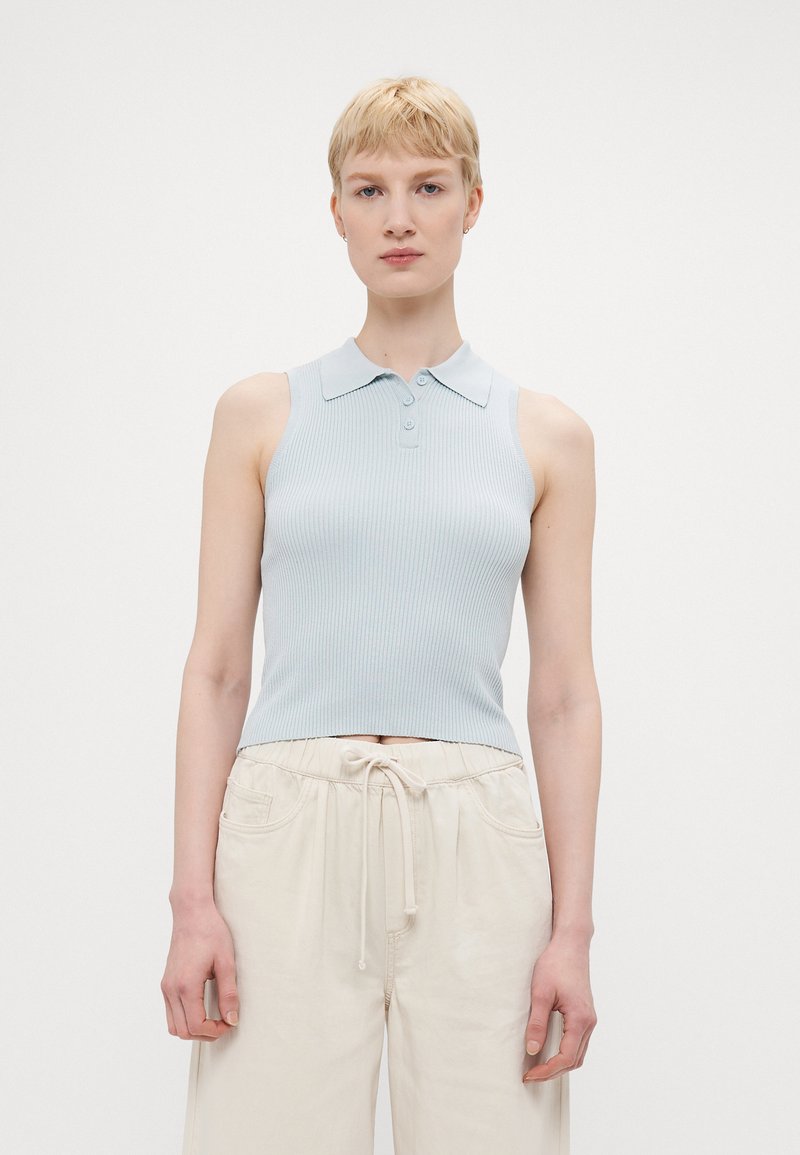 Top polo senza maniche di colore azzurro chiaro a coste con colletto e tre bottoni, abbinato a pantaloni larghi crema con vita elastica e cordino.