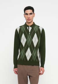 Grüner Polo-Pullover mit Argyle-Muster in Weiß und Dunkelgrün, mit Knopfkragen, gerippten Bündchen und Saum; aus weichem Strickstoff gefertigt.