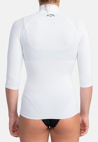 Vit rash guard med långa ärmar, hög krage och en åtsittande design. Tyget ser slätt ut med minimala sömmar. Logotyp på baksidan.