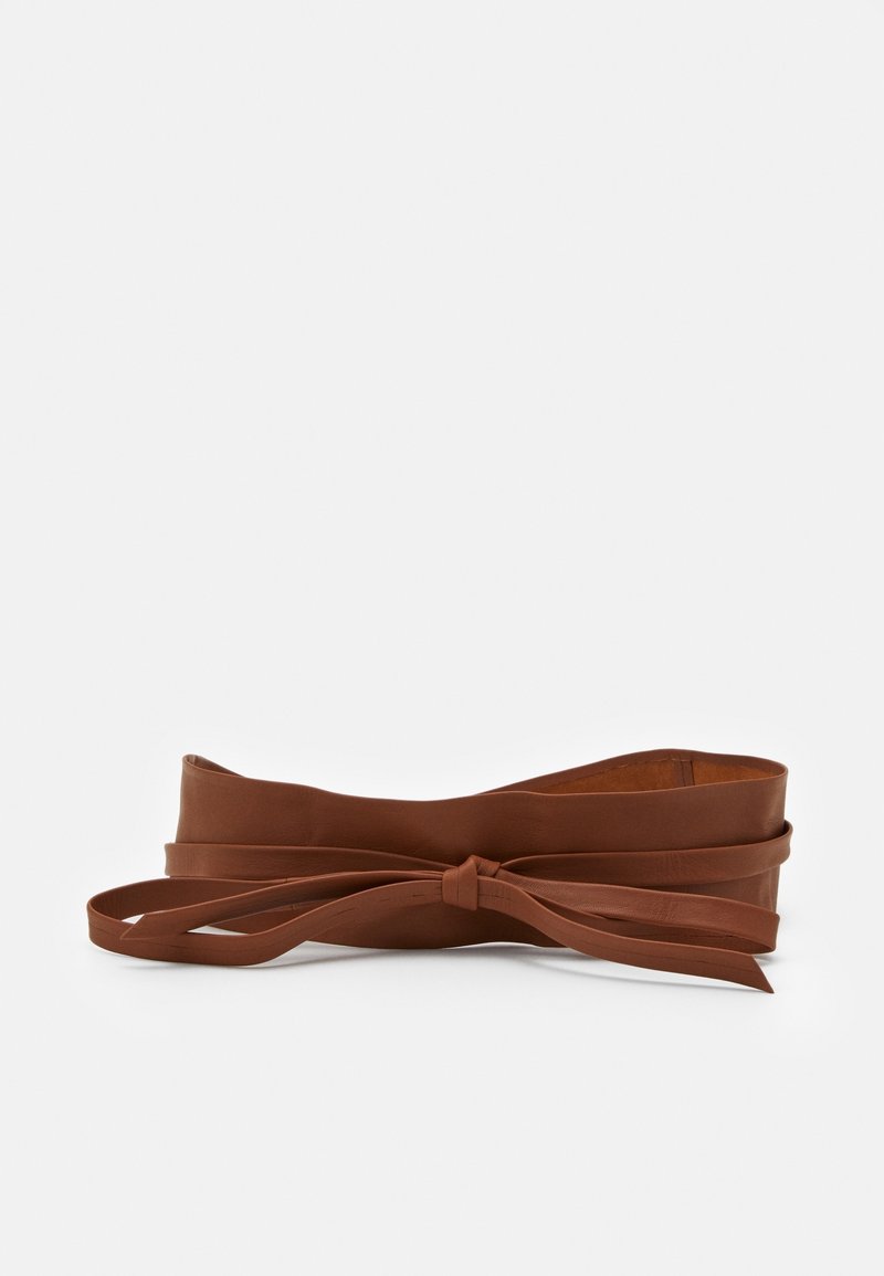Large ceinture en cuir marron de style enveloppant avec un nœud noué à l'avant, présentée sur un fond clair uni.