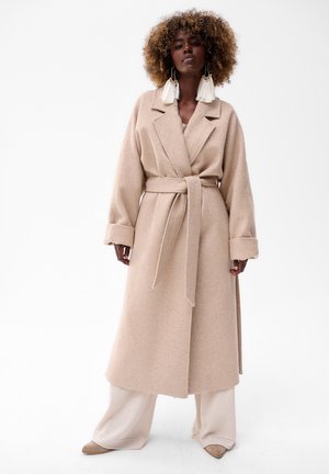 Beige Wollmischung langes Kleid mit einem gebundenen Bund, breiten Revers und hochgekrempelten Ärmeln, kombiniert mit hellbeigen weiten Hosen.