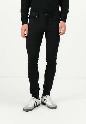 Svarta denimjeans med slim fit, fem fickor och knappstängning. Bärs med vita och grå sneakers med svarta ränder.
