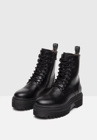 Bottes bottines en cuir noir avec bout rond, devant lacé et zip latéral; dotées d'une semelle en caoutchouc épaisse et d'une languette à l'arrière.