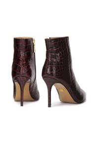 Botines de piel de cocodrilo en burdeos, con puntera afilada, tacones de aguja altos y cierre lateral. Presentan un detalle de superficie texturizada.