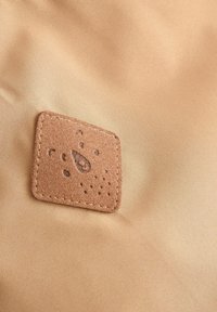 Tela color beige con un parche cuadrado de cuero marrón claro que presenta un diseño en relieve y costura alrededor de los bordes.