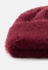 Căciulă din blană burgundă, cu o textură moale și pufoasă, având o formă rotundă și un căptușel interior neted pentru confort.