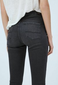 Jeans de mezclilla negra con un diseño ajustado, dos bolsillos traseros y una textura sutil. Cintura alta con una etiqueta en la parte trasera de la cintura.