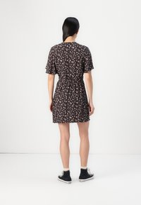 Robe noire à motif floral, à manches courtes, taille cintrée et accents froncés. Associée à des baskets montantes noires et des jambes de couleur de peau visible.