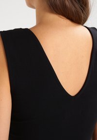 Top noir ajusté avec un décolleté en V profond à l'arrière, fabriqué en tissu lisse, doté de bretelles légèrement larges et d'une silhouette ajustée.