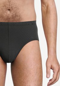 Slip da bagno neri con motivo esagonale, caratterizzati da una superficie liscia e un elastico in vita. Etichetta del logo posizionata sull'anca.