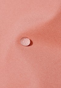Koralfarbenes Gewebe mit glatter Textur, das eine klare Regentropfenperle zeigt. Das Material ist leicht und leicht reflektierend, was die Wasserbeständigkeit verbessert.