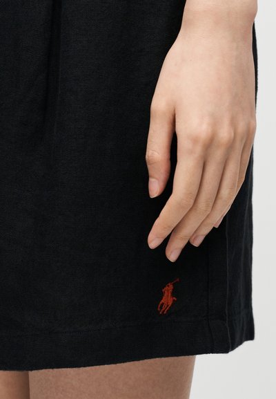 Χέρι που ακουμπά δίπλα σε μαύρο ύφασμα με μικρό κόκκινο κεντημένο σχέδιο ενός ατόμου που ιππεύει άλογο κοντά στο στρίφωμα.