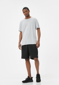Camiseta de manga corta gris claro combinada con pantalones cortos negros. El conjunto presenta un ajuste relajado y una tela suave. Zapatillas deportivas negras completan el look.