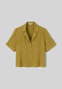 Chemise à manches courtes, de couleur vert olive, en tissu léger. Présente un col et cinq boutons sur le devant, avec un ourlet droit.