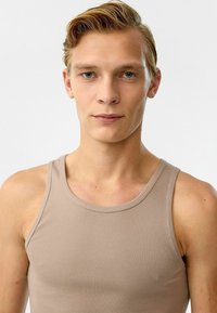 Beige geribbelde tanktop met brede schouderbanden, met een aansluitend ontwerp en een gladde textuur. Geen noemenswaardige patronen of accenten.