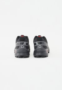 Black running shoes with a textured upper, featuring gray accents and Salomon branding. The sole has a rugged tread pattern for traction.