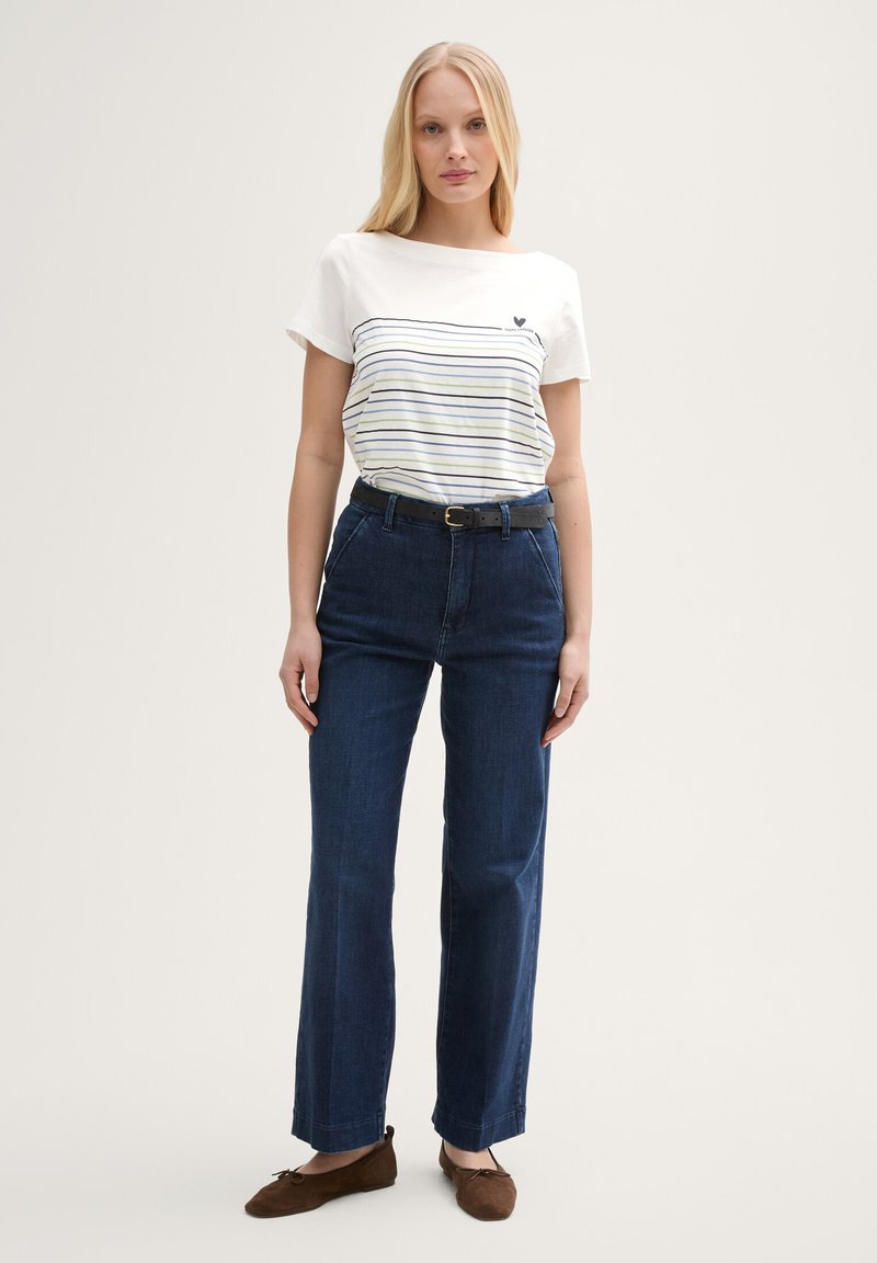 T-shirt blanc avec motif rayé bleu marine, associé à un jean bleu foncé taille haute et des chaussures plates marron. Une ceinture noire accentue la taille.