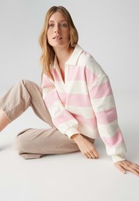 Gestreepte trui in crème en lichtroze, met een kraag en een losse pasvorm. Gecombineerd met lichtbeige cropped broek.