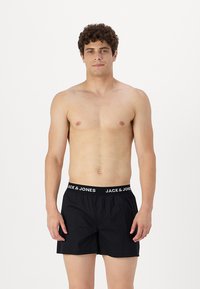 Črne bokserice z elastiko v pasu, ki nosijo blagovno znamko "JACK & JONES", iz gladke tkanine, ohlapnega kroja in enostavnega dizajna.