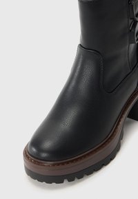 Black leather ankle boot with chunky brown platform sole and textured grip, featuring side lace-up detail and smooth rounded toe.