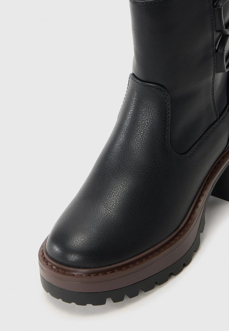 Schwarze Leder-Stiefelette mit robustem braunem Plattformsohle und strukturiertem Grip, mit seitlichem Schnürdetail und glattem, abgerundetem Zehenbereich.