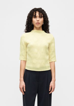 Κίτρινο τοπ με υφή, με κοντά μανίκια, ψηλό λαιμό και εφαρμοστή γραμμή, σε συνδυασμό με σκούρο, φαρδύ παντελόνι.