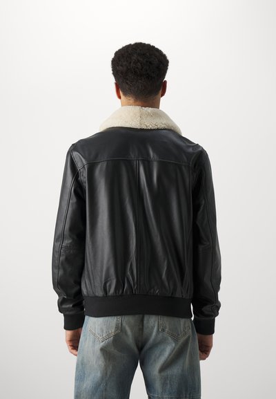 Black leather bomber jacket with a cream shearling collar, ribbed cuffs, and waist; features a smooth texture and casual fit.