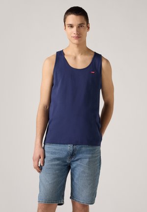 Navy blue cotton tank top with a rounded neckline and a small red logo on the chest, paired with light blue denim shorts.