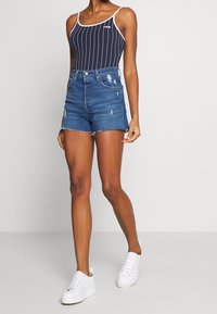 Body de rayas marineras con tirantes finos, combinado con shorts de mezclilla desgastados. Zapatillas blancas completan el conjunto. Look casual de verano.