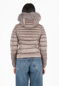 Giacca imbottita beige con cappuccio in pelliccia sintetica, caratterizzata da un design trapuntato orizzontale e polsini elasticizzati, abbinata a jeans in denim.