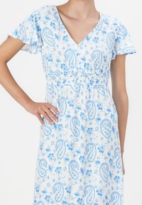 Robe à motifs paisley bleu et blanc avec un décolleté en V, des manches courtes évasées, une taille élastique et des détails de boutons à l'avant.