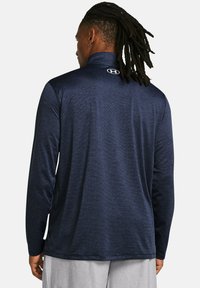 Navyblaues langärmliges Sportoberteil mit hohem Kragen, strukturiertem Stoff und Logo auf der Rückseite. Geeignet für Sport und Freizeit.