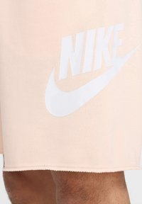 Calções Nike em tecido pêssego claro com um logótipo branco proeminente. O design apresenta uma textura suave e uma borda rematada.