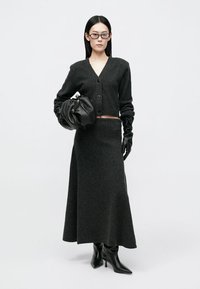 Σκούρο γκρι μάλλινο κα cardigan με κούμπωμα, συνοδευμένο από μια ταιριαστή μακριά φούστα. Το μοντέλο κρατά μια μαύρη τσάντα και φορά δερμάτινα γάντια και μπότες.