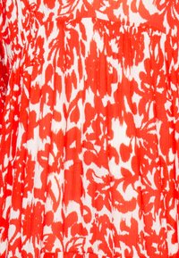 Tissu rouge et blanc avec des motifs floraux abstraits et des coups de pinceau, montrant une texture plissée et des plis verticaux.