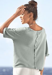 Hellgrüner Strickpullover mit kurzen, umgeschlagenen Ärmeln, lockerer Passform und Knopfdetails im Rücken. Der Stoff wirkt weich und strukturiert.