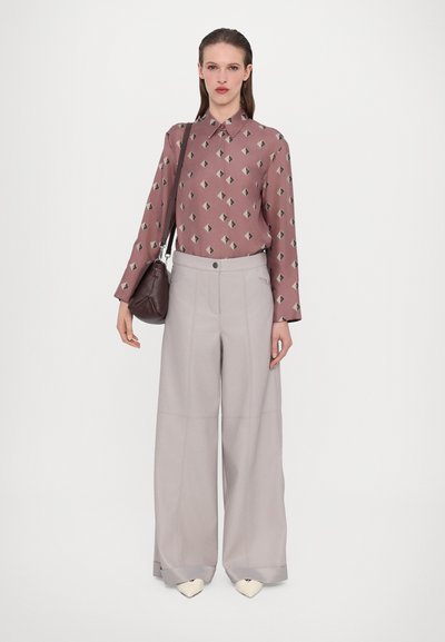 Långärmad, ljusrosa blus med diamantmönster; vida, ljusgrå byxor; liten brun väska; krämfärgade spetsiga skor.