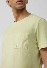 Lichtgele katoenen T-shirt met een ronde hals, voorzien van een vierkant borstzakje en een klein logo op het zakje. Glad textuur.