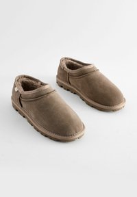 Chaussures slip-on en daim marron avec une doublure intérieure douce, un bout rond et une semelle en caoutchouc texturée, dotées d'un design à profil bas.