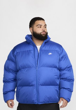 Plavi pufasti kaput od najlona, s visokim ovratnikom, zatvaranjem na zipper i Nike logotipom na lijevoj strani prsiju; kviltana tekstura i oversized kroj.