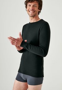 Camisetta nera a maniche lunghe in tessuto liscio, con scollo rotondo e polsini ai polsi, abbinata a boxer grigi.