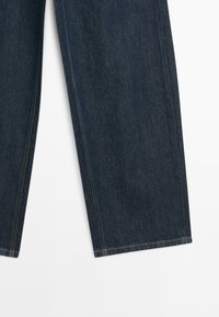 Dunkelblaue Denim-Jeans mit geradem Schnitt und sichtbaren orangefarbenen Nähten auf weißem Hintergrund.
