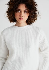 White, ribbed sweater with a round neckline and long sleeves, featuring a soft texture and straight fit, suitable for layering or standalone wear.