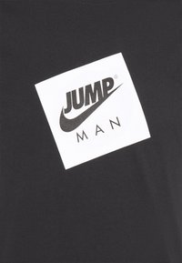 Černé bavlněné tričko s bílým obdélníkovým grafickým prvkem, na kterém je text "JUMP" a "MAN" černou barvou, spolu s logem Nike swoosh.