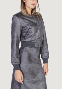 Chaqueta bomber gris cortada hecha de una tela texturizada, con cuello redondo, cierre de botón en el frente y puños acanalados.