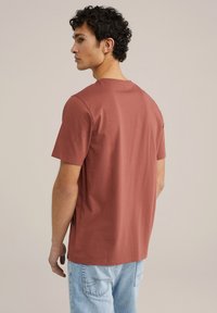 Roodkleurig katoenen t-shirt met een ronde hals, korte mouwen en een rechte zoom, gedragen met lichtblauwe spijkerbroek. Geen zichtbare patronen.