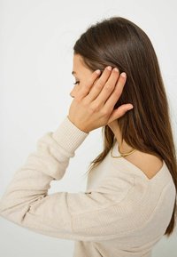 Beige ribbat tröja med delvis axelbar design, med en texturerad yta och ett subtilt guldhalsband.