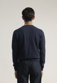 Suéter navy con cuello redondo y puños acanalados, hecho de una tela suave. Combinado con pantalones oscuros, mostrando una silueta simple y ajustada.