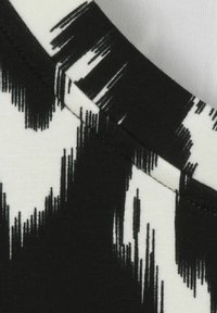 Tissu à motifs noir et blanc avec une texture douce, arborant des rayures dentelées sur un fond contrasté, présentant un gros plan de l'encolure.